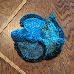 Peut inclure: Un tapis crocheté en forme de fleur bleu et vert avec une surface texturée.