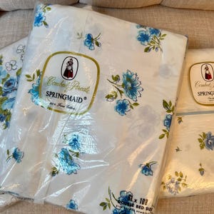 May include: White and blue floral Springmaid Combed Percale double bed sheet set. The sheets are packaged in clear plastic and feature a repeating pattern of blue flowers and green leaves. The packaging includes the Springmaid logo and product information.