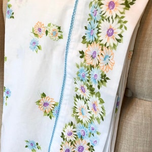 May include: White fitted sheet with a blue and white floral pattern. The sheet has a blue trim with a white scalloped edge.