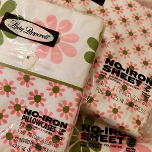 May include: A set of pink and green floral patterned bed sheets and pillowcases from Lady Pepperell. The packaging includes a full fitted sheet, a full flat sheet, and two standard pillowcases. The sheets are labeled "No-Iron" and are made of 50% Dacron polyester and 50% cotton. The fitted sheet is for a 54x75 inch mattress.