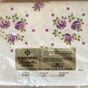 Puede incluir: Una s&aacute;bana de algod&oacute;n blanca con un estampado floral morado y lunares blancos. La s&aacute;bana est&aacute; empaquetada en pl&aacute;stico y tiene una etiqueta que dice "CANNON Monticello Muslin" y "CANNON MILLS, INC., NEW YORK, N.Y. 10020".