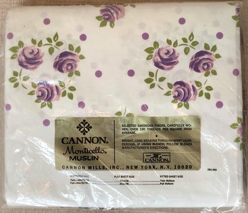 Puede incluir: Una s&aacute;bana de algod&oacute;n blanca con un estampado floral morado y lunares blancos. La s&aacute;bana est&aacute; empaquetada en pl&aacute;stico y tiene una etiqueta que dice "CANNON Monticello Muslin" y "CANNON MILLS, INC., NEW YORK, N.Y. 10020".