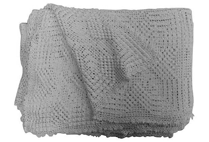 May include: A white crocheted baby blanket with a delicate pattern. The blanket is folded in half and has a soft, textured surface.