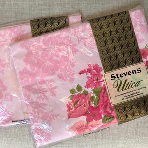 May include: Two pink floral flat sheets in plastic packaging. The packaging has a gold label with the text "Stevens Utica" and "Fine Combed Percale with Exclusive Detail Finish. One Sheet Full/Flat 81 x 108 Size. Wash Before Using."
