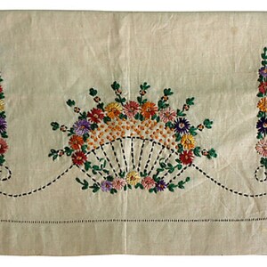 May include: A white linen pillowcase with embroidered floral designs in shades of green, orange, yellow, purple, and pink. The flowers are arranged in a fan shape in the center and two vertical lines on either side.