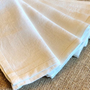 May include: A stack of white linen napkins with a subtle embossed pattern and a stitched edge.