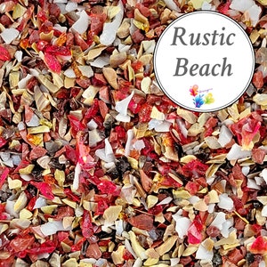 Op de afbeelding: Close-up van een mix van stukjes gebroken glas in verschillende kleuren, waaronder rood, wit, bruin en zwart. De tekst "Rustic Beach" staat in een witte cirkel. Geschikt voor knutselprojecten.
