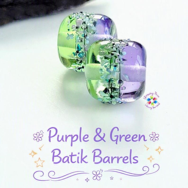 May include: Two barrel-shaped glass beads featuring a split color design of translucent lime green and purple. A textured band of iridescent, multi-colored glass fragments encircles the center. Text reads: Purple & Green Batik Barrels.