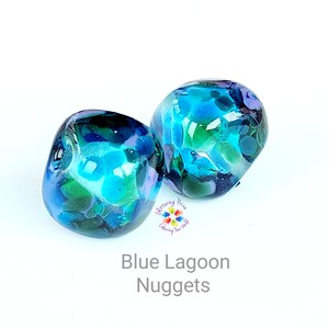 May include: Two glass nuggets with a blue lagoon design. The nuggets are a mix of blue, green, and white colors. The text "Blue Lagoon Nuggets" is at the bottom of the image.