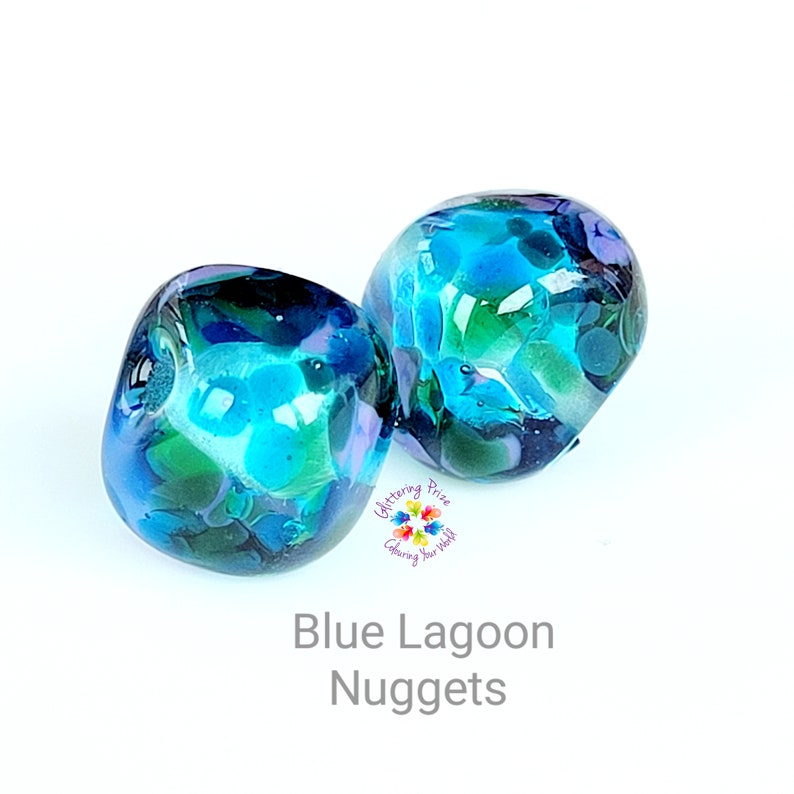 May include: Two glass nuggets with a blue lagoon design. The nuggets are a mix of blue, green, and white colors. The text "Blue Lagoon Nuggets" is at the bottom of the image.