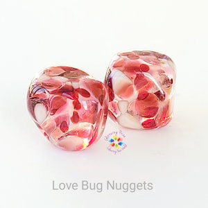 May include: Two red and white glass nuggets with a textured surface. The nuggets are translucent and have a speckled appearance.