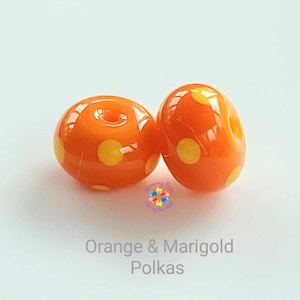 May include: Two orange glass beads with yellow polka dots. The beads are round and have a hole in the center for stringing.