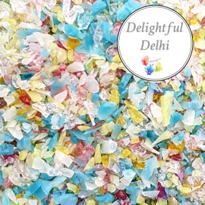 Puede incluir: Primer plano de piezas de vidrio coloridas e iridiscentes, perfectas para manualidades o decoración. Las piezas de vidrio son de diversas formas y tamaños, con tonos de azul, amarillo, rosa y blanco.