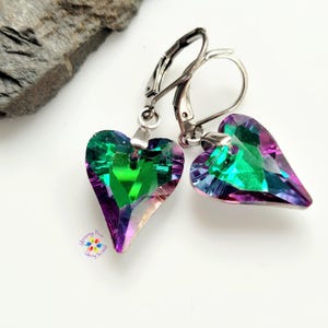 May include: A pair of silver heart-shaped earrings with iridescent green, purple, and blue crystals.