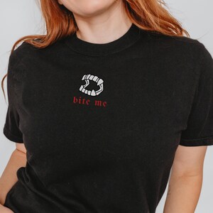 May include: Black t-shirt with a white graphic of vampire fangs and the text "bite me" in red.