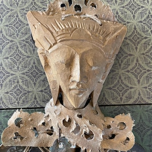 May include: A wooden sculpture of a face with a crown, carved in a triangular shape. The sculpture is painted gold and has intricate details.