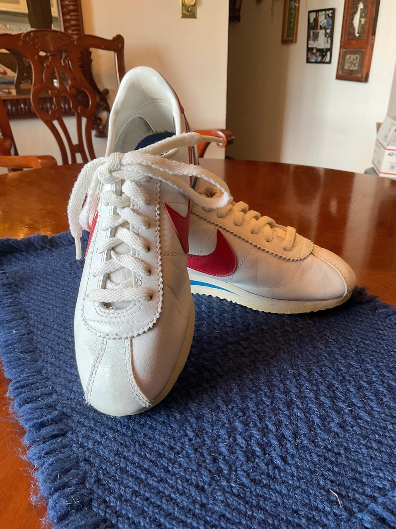 May include: A pair of white leather trainers with red and blue accents. The trainers have white laces and a white sole.
