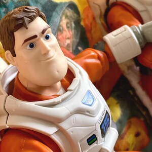 May include: A Buzz Lightyear action figure, featuring a detailed face and a white and orange spacesuit. The figure has a white chest plate with the word "LIGHTYEAR" and the number "15" printed on it. The background is a colorful, patterned fabric.