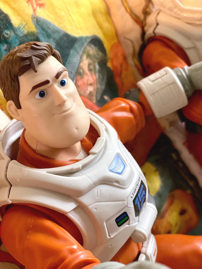 May include: A Buzz Lightyear action figure, featuring a detailed face and a white and orange spacesuit. The figure has a white chest plate with the word "LIGHTYEAR" and the number "15" printed on it. The background is a colorful, patterned fabric.