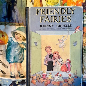May include: Vintage book cover titled "Friendly Fairies" by Johnny Gruelle. The cover features an illustration of children and fairies in a whimsical scene. The book is set against a backdrop of colorful Halloween-themed fabric.