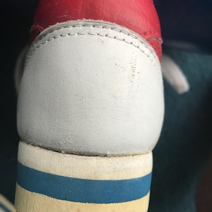 May include: Close-up of a white leather Nike shoe with a red leather upper and blue and white trim. The Nike logo is visible on the red upper.