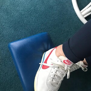 May include: White leather trainers with a red and blue Nike swoosh logo. The shoes have white laces and a white rubber sole.