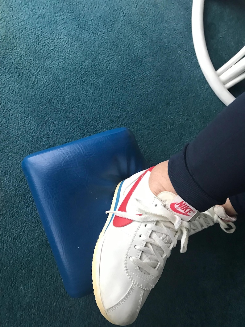 May include: White leather trainers with a red and blue Nike swoosh logo. The shoes have white laces and a white rubber sole.