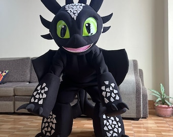 May include: A full-body black dragon costume featuring large bright green eyes, a pink mouth, and white triangular scale patterns on the head, arms, and legs. The suit includes pointed ears, horns, and large wings extending from the back.