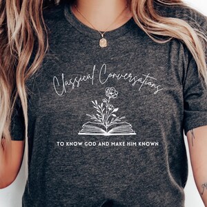 May include: A heather gray t-shirt with a white graphic design of an open book with flowers and the text "Classical Conversations" and "To know God and make Him known."