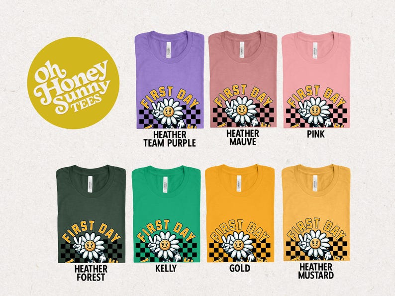 May include: A set of ten t-shirts in various colors featuring a graphic of a smiling flower with the text "First Day" in a checkered background. The t-shirts are available in Heather Team Purple, Heather Mauve, Pink, Heather Forest, Kelly, Gold, and Heather Mustard.