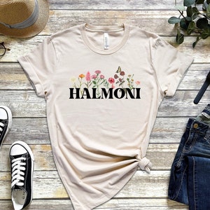 May include: A beige t-shirt with a floral design and the word "HALMONI" printed in black.