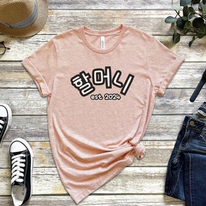 May include: A pink t-shirt with the Korean text "하이" and the text "est 2024" printed on the front.