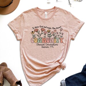 May include: A pink t-shirt with a floral design and the text "To know God and make Him known COMMUNITY Classical Conversations Jackson, TN".
