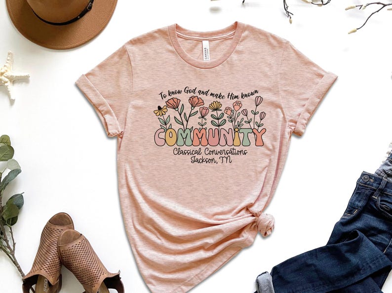May include: A pink t-shirt with a floral design and the text "To know God and make Him known COMMUNITY Classical Conversations Jackson, TN".