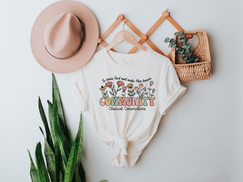 May include: A white t-shirt with a floral design and the text "To know God and make Him known COMMUNITY Classical Conversations".