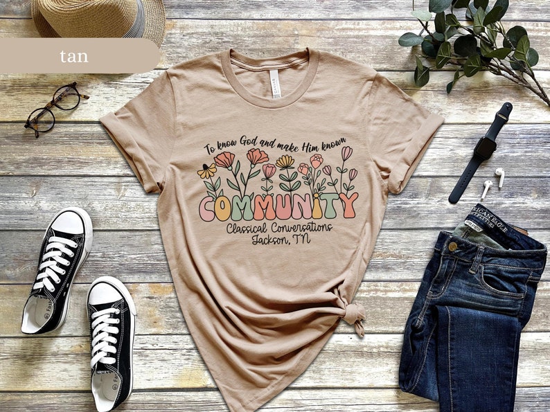 May include: Tan t-shirt with a floral design and the text "To know God and make Him known COMMUNITY Classical Conversations Jackson, TN".