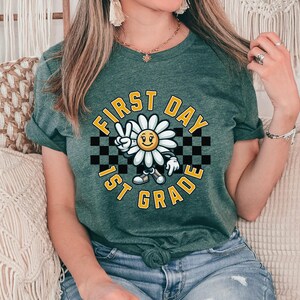 May include: A green t-shirt with a white daisy graphic and the text "First Day 1st Grade" in a black and white checkered pattern.