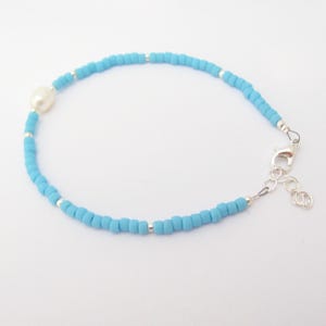 May include: A delicate blue beaded bracelet with a single white pearl accent and a silver clasp.