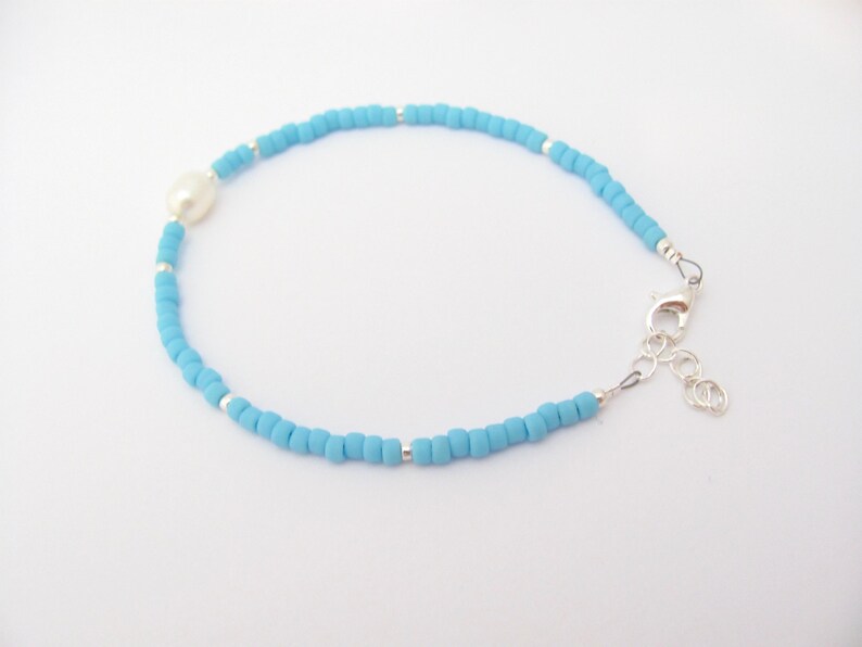 May include: A delicate blue beaded bracelet with a single white pearl accent and a silver clasp.