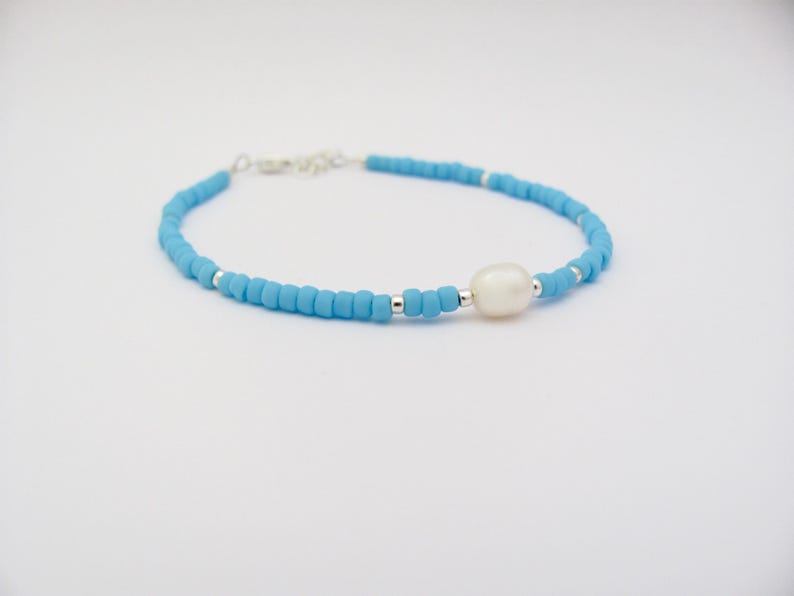 May include: A delicate blue beaded bracelet with a single white pearl charm.