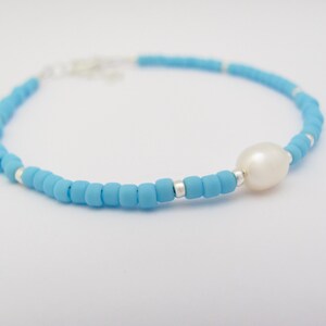 May include: A delicate blue beaded bracelet with a single white pearl charm.