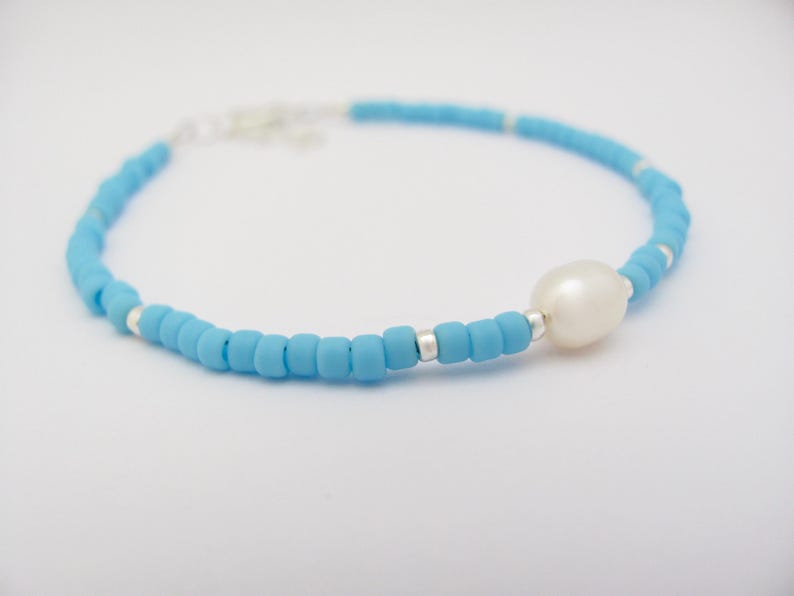 May include: A delicate blue beaded bracelet with a single white pearl charm.