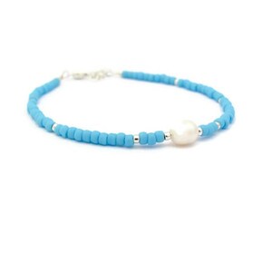 May include: A delicate bracelet made with light blue beads and a single white pearl. The bracelet is strung on a silver chain.