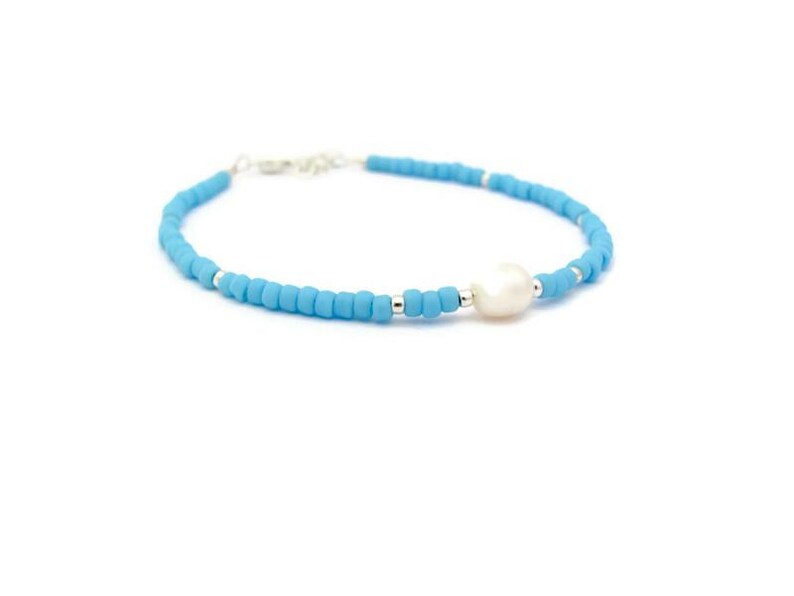 May include: A delicate bracelet made with light blue beads and a single white pearl. The bracelet is strung on a silver chain.