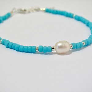 May include: A turquoise beaded bracelet with a single white pearl charm.