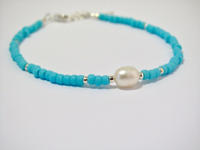 May include: A turquoise beaded bracelet with a single white pearl charm.