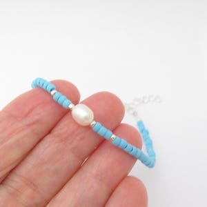 May include: A delicate bracelet made with tiny light blue beads and a single white pearl. The bracelet is secured with a silver chain.
