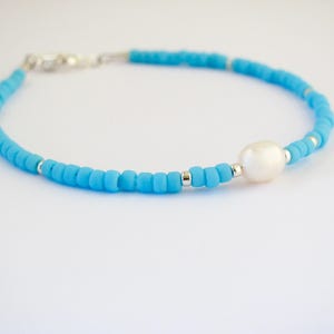 May include: A delicate blue beaded bracelet with a single white pearl accent. The bracelet is made with small, round beads and has a silver clasp.