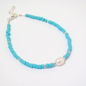 May include: A turquoise beaded bracelet with a single white pearl accent. The bracelet has a silver clasp.