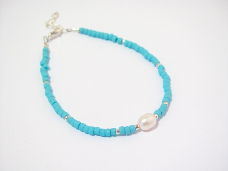May include: A turquoise beaded bracelet with a single white pearl accent. The bracelet has a silver clasp.